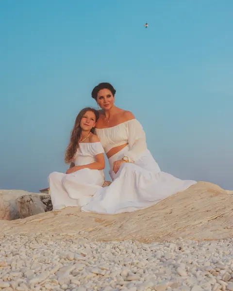 Mother and daughter dressed in white on the rocks at sunset