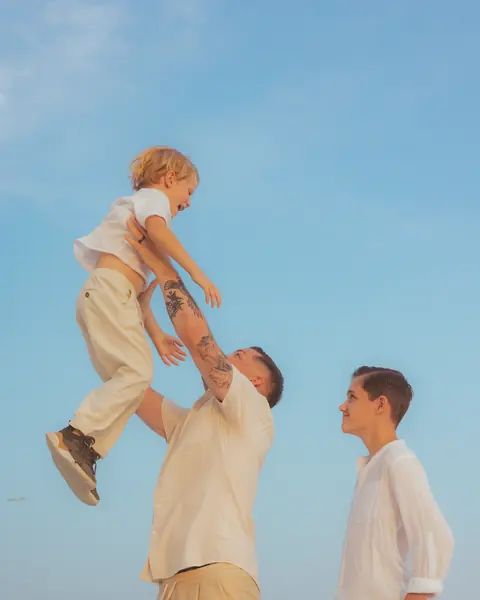 Father throwing his little son into the air under a blue sky