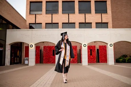 Graduate in cap and gown walking across the university campus