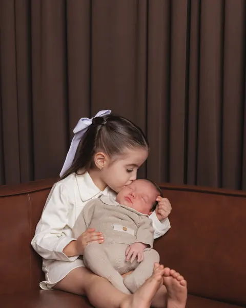 Big sister kissing her newborn brother on the studio sofa