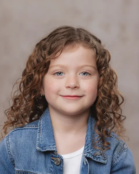 Girl with curly hair in a denim jacket smiling at the camera