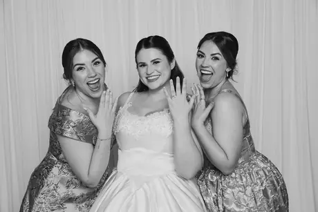 Woman in a white gown laughing with two friends in patterned dresses