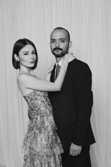 Couple in formal wear standing close against a draped backdrop