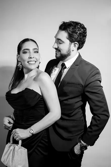 Woman in a black strapless dress smiling while a man in a suit looks at her