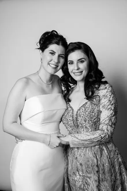 Woman in a white strapless gown embracing a woman in a beaded gown