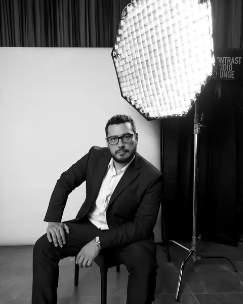 Black and white portrait of Roel Tobias seated in his studio beside a softbox