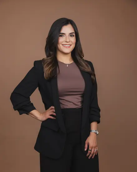 Professional portrait of a woman in a black blazer against a tan backdrop