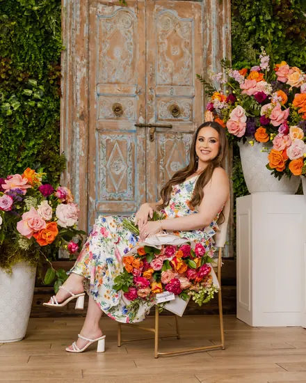 Woman in a floral dress seated among flower arrangements at an event