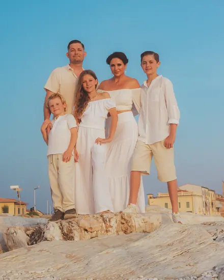 Family of five dressed in white standing on the rocks under a clear sky