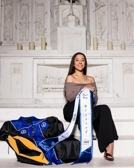 Graduate with her stole and gown, seated in front of a carved white altar